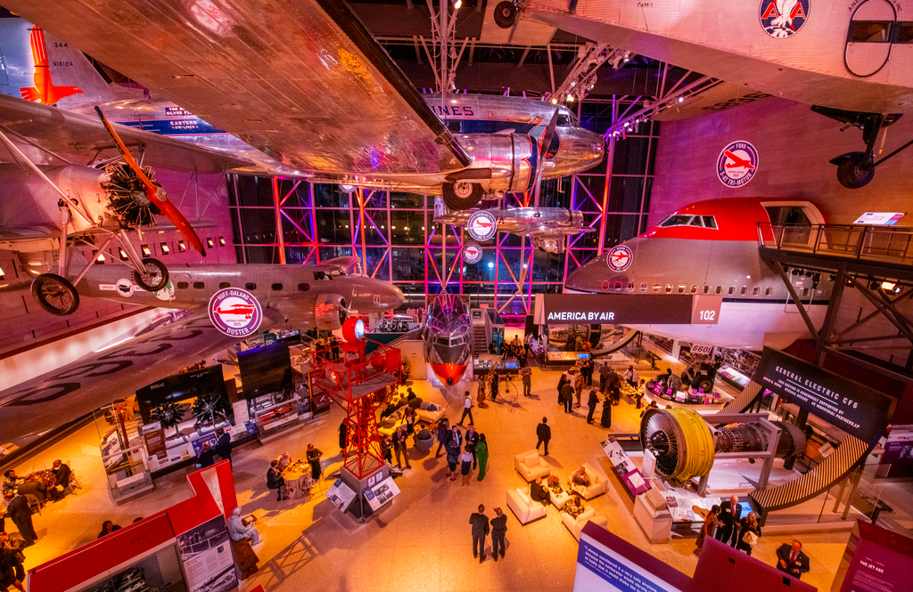 A gallery with planes hanging from the ceiling. It's set up for a special event.