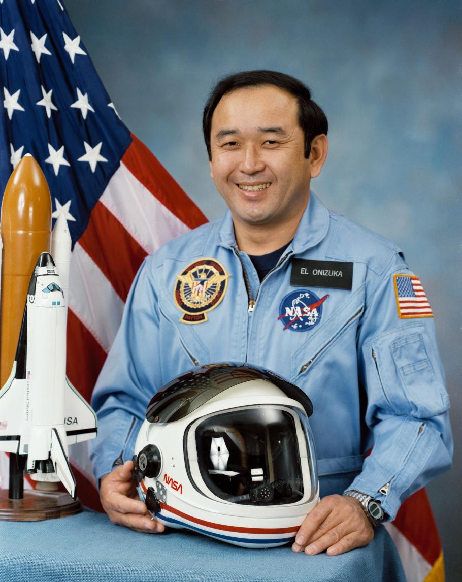A man smiles at the camera. There is an American flag in the background.