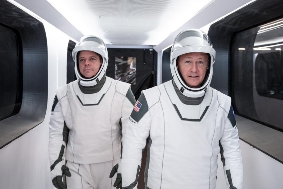 two astronauts in white spacesuits walk down hallway