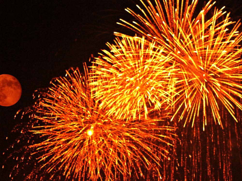 A red-colored full moon next to many red, yellow, and orange fireworks.