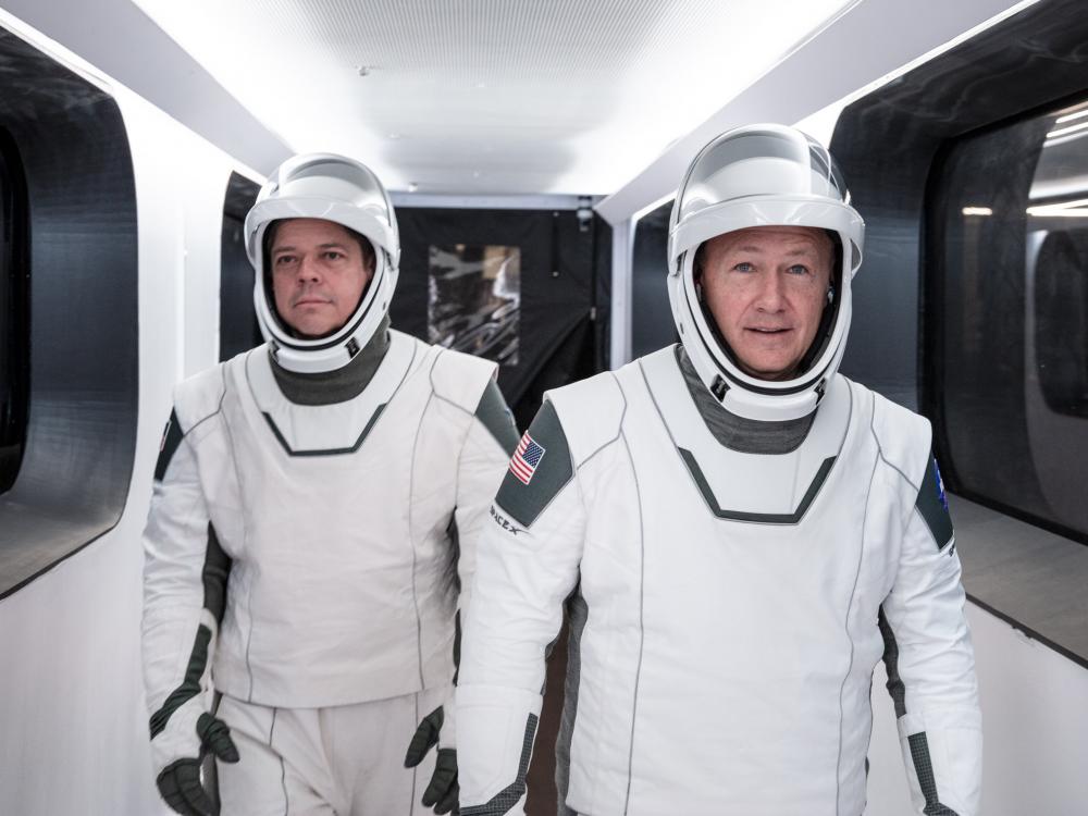 two astronauts in white spacesuits walk down hallway