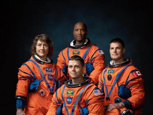 Four astronauts in orange flight suits pose for a photo as a crew.