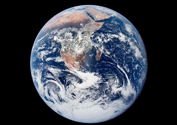 A complete circle with swirling clouds above landmasses, the Earth is seen from above. 