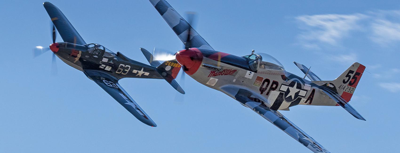 The dark blue P-51D Man O War plane races through the sky alongside Pretty Polly, a P-63C plane with a grey fuselage and blue-striped wings.